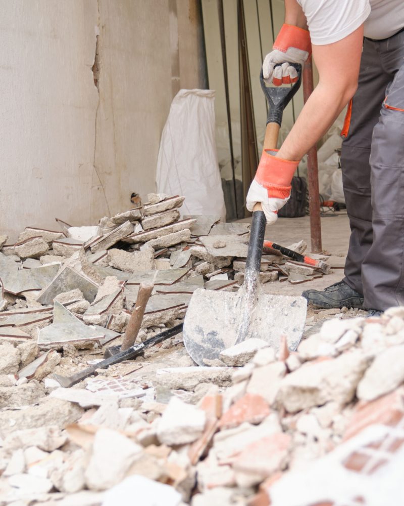 Unrecognizable builder collecting construction debris with a shovel. House renovation.